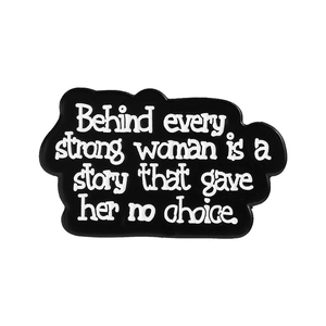 Spilla in smalto con frase Behind every strong woman is a story su sfondo bianco pulito