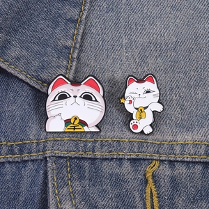 Détail de deux épingles en émail Maneki Neko avec cloches dorées sur fond en denim