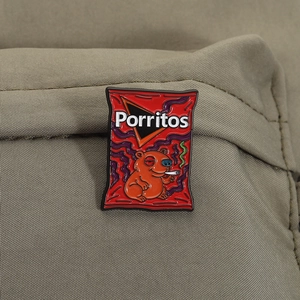 Macro view of red snack bag enamel pin with parody bear illustration on khaki fabric