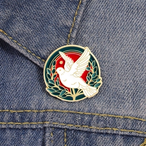 Vista detallada del broche esmaltado de paloma con rama de olivo sobre tela denim azul