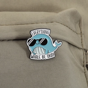 Detail of cute whale enamel pin with 'EVERYTHING WHALE BE OKAY' text on canvas bag