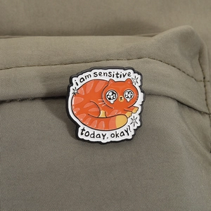 Cute orange tabby cat enamel pin with I am sensitive today text on green fabric