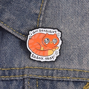 Cute orange cat enamel pin with I am sensitive today text on denim jacket