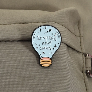 Close-up of light blue enamel light bulb brooch with Inspire And CREATE text on a backpack