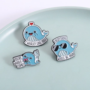Three cute blue whale enamel pins with funny puns on a light blue ceramic tray