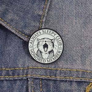 Vintage enamel lazy cat brooch featuring Always Sleepy Club text on a denim jacket