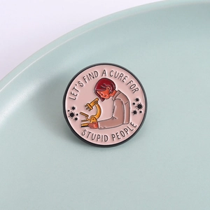 Enamel microscope brooch with 'Let's Find A Cure For Stupid People' slogan on pink background
