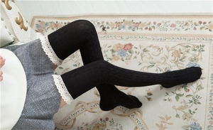 Close-up of black cable knit over-knee socks with delicate cream lace trim detail