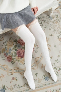 Detail of white cable knit over-the-knee socks with delicate lace trim at the cuff