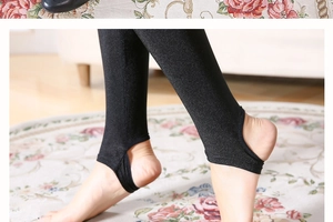 Detailed view of black stirrup leggings showing elastic glossy fabric and foot strap