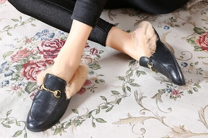 Close-up of black leather mule with gold horsebit buckle and warm plush lining
