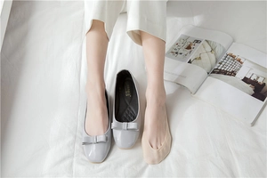 Close-up of light gray patent leather ballet flats with bow and beige invisible socks