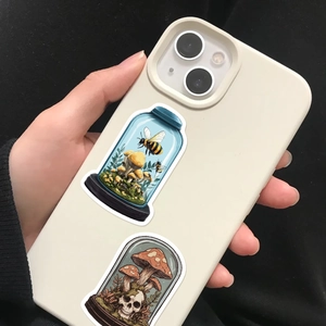 Close-up of decorative bee and skull bottle stickers on a mobile phone case surface