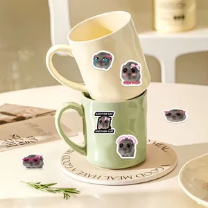 Ceramic mugs with sad hamster stickers and large round handles in a home setting