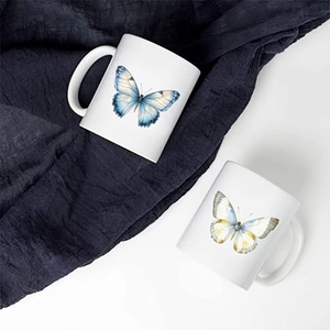 Close-up of white ceramic mugs featuring colorful hand-painted watercolor butterfly designs