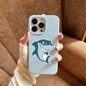 Light blue iPhone case with a cartoon shark design held over a brown checkered background