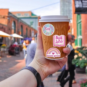 Dettaglio di adesivi rosa Lover e Book Girlie su una tazza da caffè in ambiente esterno