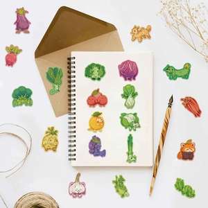 Flat lay of cartoon vegetable and fruit animal stickers on white desk with stationery