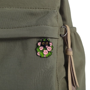 Enamel pin featuring a black cat hiding in flowers, pinned on a green backpack pocket