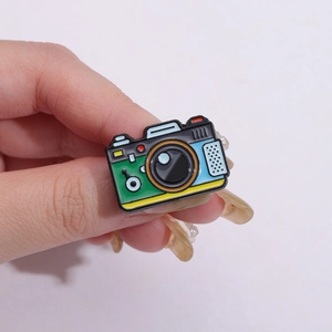 Retro camera enamel pin in green and blue colors shown being held in hand