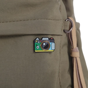 Retro colorful camera enamel pin on green backpack pocket with detailed metal texture