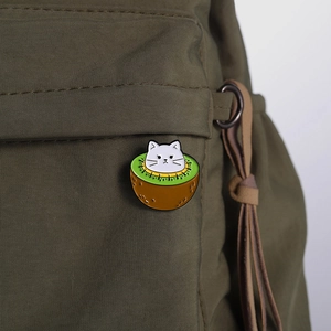 Creative cartoon cat kiwi fruit enamel brooch pin displayed on a green canvas backpack
