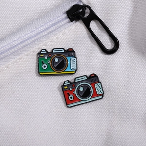 Set of two vintage camera enamel pins in red and green on a white canvas backpack