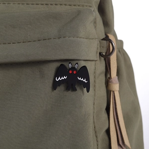 Gothic Mothman enamel pin with red eyes and white feather texture on a green backpack