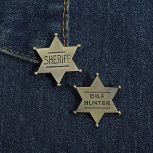 Close-up of bronze hex star badges with Sheriff and Dilf Hunter text on denim