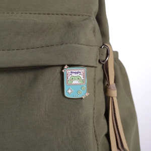 Mint green frog game console enamel brooch pinned on a military green canvas backpack