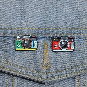 Close-up of vintage camera enamel pins in colorful lacquer on a denim jacket pocket