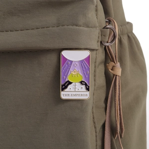 Tarot-inspired enamel pin featuring a frog emperor design on dark green nylon background