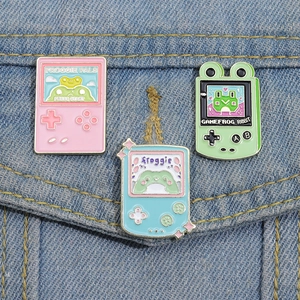 Retro game console enamel pins featuring cute pixel frogs on a denim jacket pocket