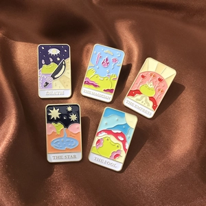 Detailed close-up of tarot frog enamel pins set on a luxurious brown satin fabric