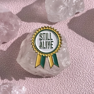 Détail d'une broche en émail en forme de médaille avec texte Still Alive sur cristal
