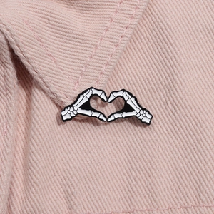 Detail einer Emaille-Brosche mit Skeletthänden in Herzform auf rosa Denim-Stoff fixiert