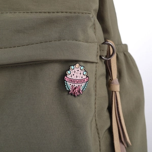 Detail of Lunar Witch enamel pin with crystals and moon phases on green canvas bag