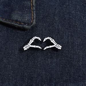 Detailansicht der Emaille-Pins in Form von Skeletthänden auf dunkelblauem Denim