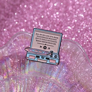 Detail shot of a retro pink and blue enamel record player brooch with song lyrics