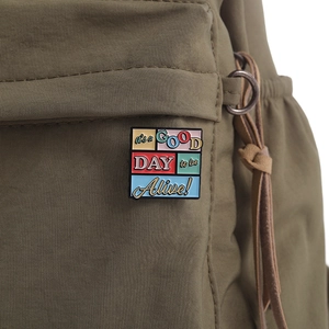 Détail de la broche en émail coloré avec texte motivant sur un sac en toile verte