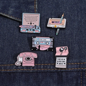 Detail of vintage pink enamel pins featuring retro record player and camera on denim