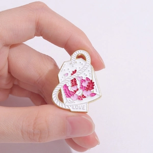 Broche de bolsita de té esmaltado con motivos de corazón y texto LOVE en mano