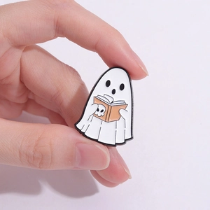 Dettaglio di una spilla in smalto a forma di fantasma che legge un libro arancione