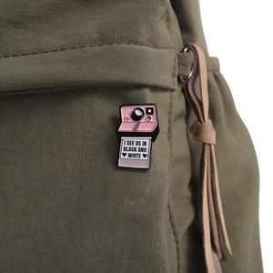 Detail of pink retro camera enamel pin with heart photo on a green canvas bag