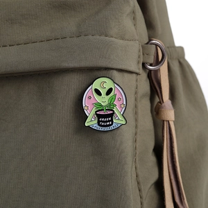 Detail einer grünen Alien-Emaille-Anstecknadel mit Green Thumb Text auf einem Rucksack