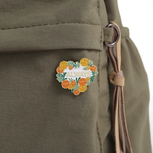 Floral heart enamel pin with 'ALWAYS' text on an olive green canvas bag