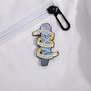 Detail of sage enamel pin with sarcastic text pinned on white canvas backpack