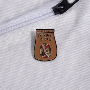 Dettaglio di una spilla smaltata a forma di sacchetto di carta su una borsa di tela bianca