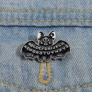 Close-up of a gothic black bat enamel pin with Ouija letters on blue denim fabric