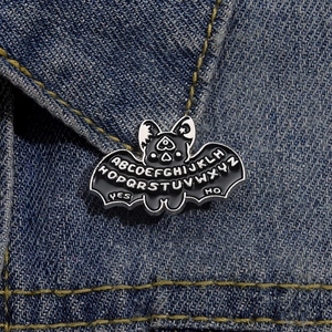 Cartoon gothic bat enamel pin with Ouija board elements on blue denim jacket